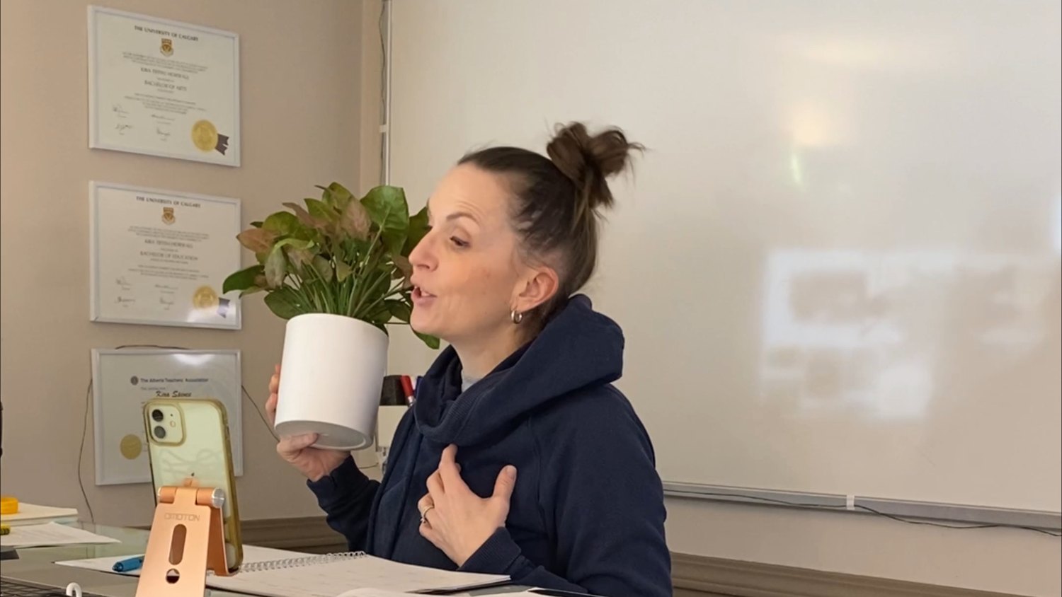 Kira teaching from her Calgary classroom, her arts and education degrees framed behind her